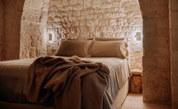 Cozy bedroom featuring a stone wall, a comfortable bed with neutral-colored bedding, and soft lighting that creates a warm atmosphere. Ideal for relaxation and a peaceful retreat.