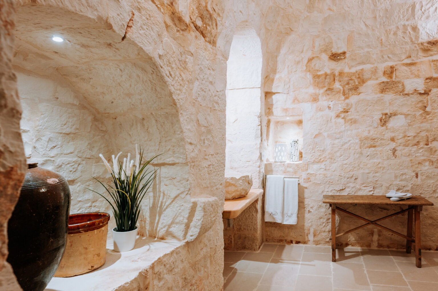 Cozy interior of a rustic stone bathroom featuring natural light, a wooden table, decorative plants, and minimalist decor, creating a serene atmosphere. | Only on SopranoVillas