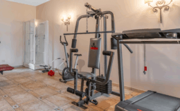 Home gym setup featuring a treadmill, multi-station weight machine, and exercise bike, with a glass shower in the background and a tiled floor. Ideal for fitness enthusiasts looking to work out at home.