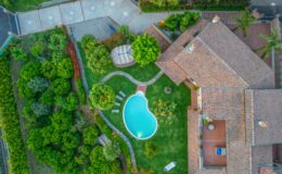 Aerial view of a luxurious residential property featuring a landscaped garden, a swimming pool in an organic shape, and a cozy gazebo. The well-maintained lawn is surrounded by lush greenery and pathways, showcasing a harmonious blend of nature and modern architecture. Ideal for outdoor relaxation and entertaining.