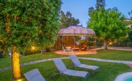 A serene garden setting featuring a gazebo surrounded by lush greenery, with comfortable seating and a small table. Lounge chairs are arranged on the manicured lawn, creating a perfect outdoor relaxation space. Soft lighting enhances the tranquil atmosphere during dusk.