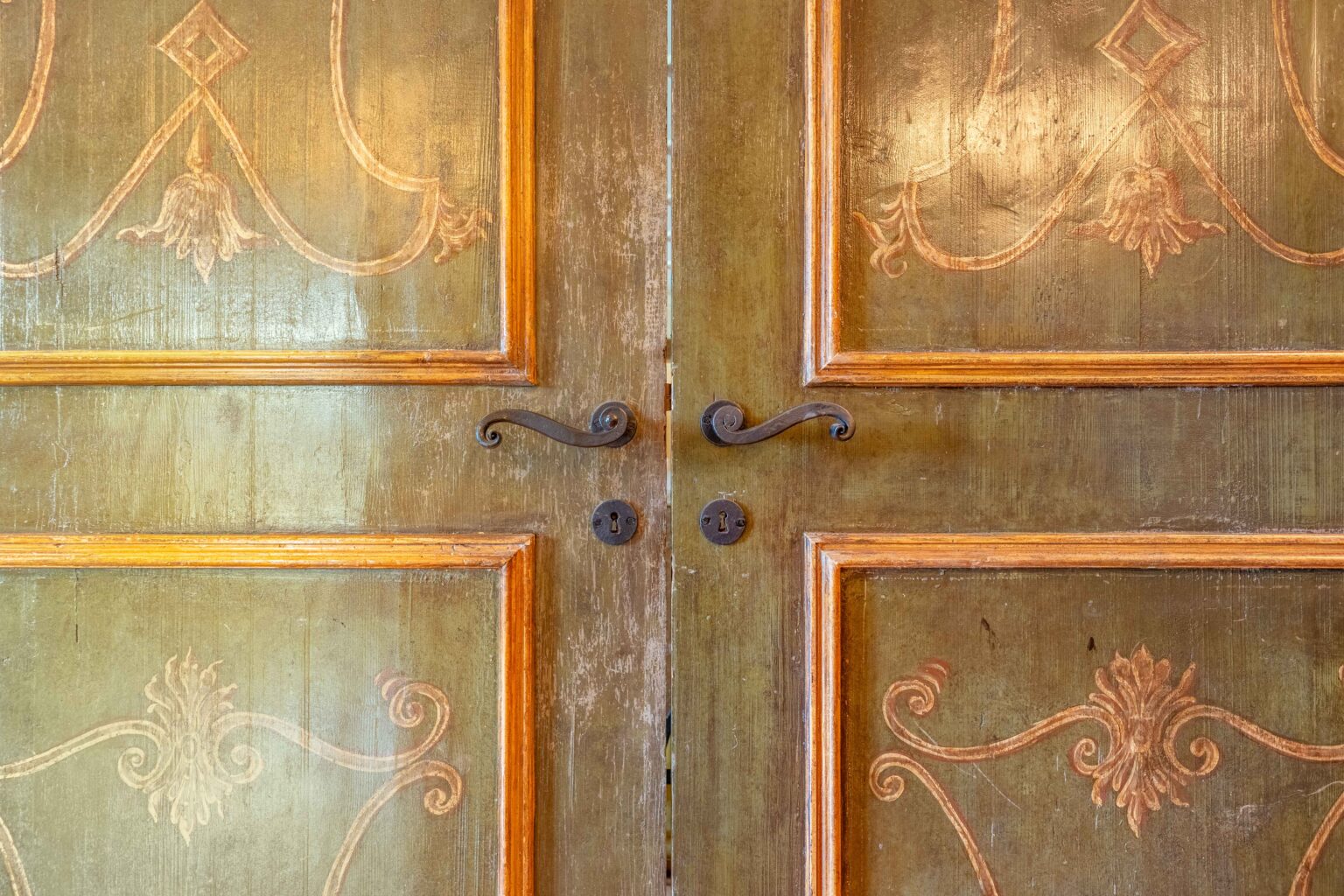 Antique wooden double doors with intricate carvings and decorative metal handles, showcasing a vintage design and aged patina. | Only on SopranoVillas