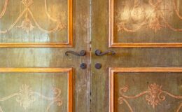 Antique wooden double doors with intricate carvings and decorative metal handles, showcasing a vintage design and aged patina.