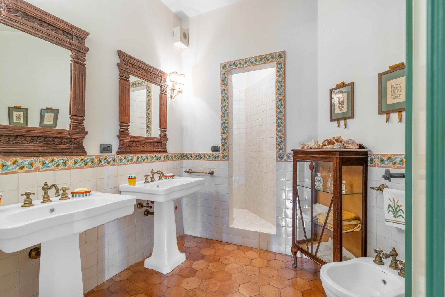 Elegant bathroom featuring vintage sinks with brass fixtures, decorative mirrors, and a walk-in shower. The room is adorned with colorful tile accents and wooden cabinetry, creating a warm and inviting atmosphere. | Only on SopranoVillas