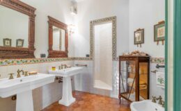 Elegant bathroom featuring vintage sinks with brass fixtures, decorative mirrors, and a walk-in shower. The room is adorned with colorful tile accents and wooden cabinetry, creating a warm and inviting atmosphere.