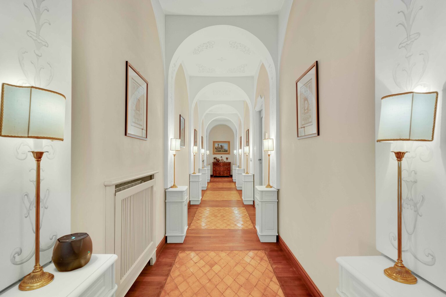 Elegant hotel corridor featuring arched ceilings, decorative artwork, and stylish lamps. The warm wooden flooring complements the light-colored walls, creating a welcoming atmosphere. | Only on SopranoVillas