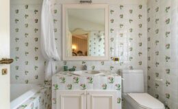 Bright and charming bathroom featuring floral-patterned tiles, a white bathtub, a modern toilet, and a stylish sink with a mirror. The decor combines classic and contemporary elements, creating an inviting atmosphere.