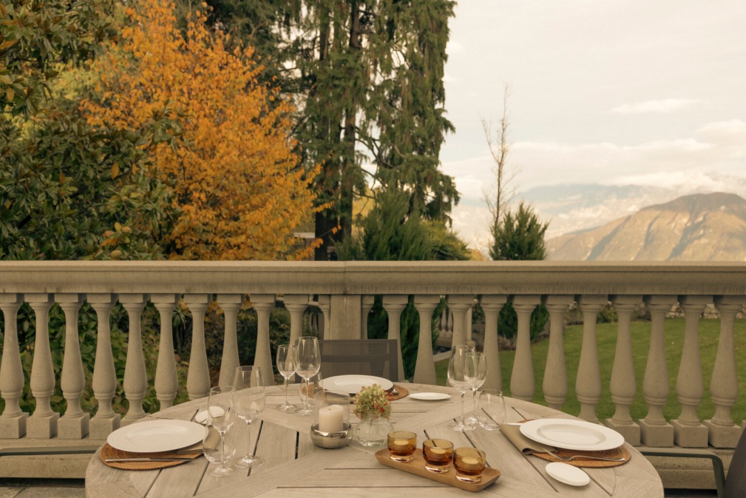Luxury villa dining terrace in Italy, featuring a beautifully set table with elegant dinnerware, surrounded by lush greenery and autumn foliage, offering stunning mountain views. Perfect for vacation rentals. | Only on SopranoVillas