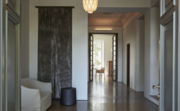 Modern interior hallway featuring a stylish sofa, a decorative wall panel, and a glimpse of a well-lit room in the background. The space showcases elegant design elements and natural light.