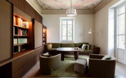 Modern living room interior featuring a cozy green sofa, stylish armchairs, and a round table, complemented by a decorative ceiling and natural light from large windows.