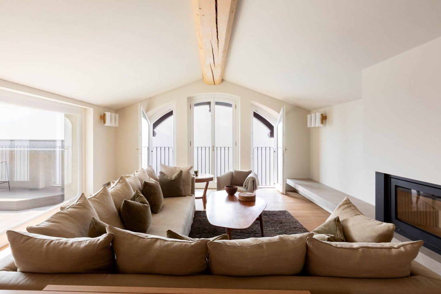 Spacious modern living room featuring a large L-shaped beige sofa, wooden coffee table, and large windows providing natural light, creating a warm and inviting atmosphere. | Only on SopranoVillas