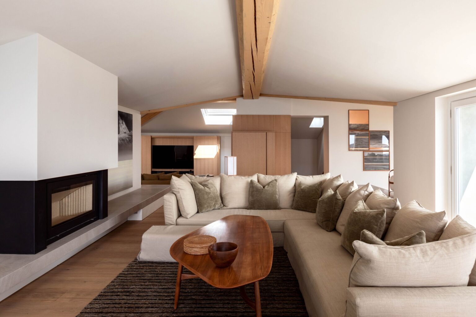 Modern living room featuring a spacious beige sectional sofa, a wooden coffee table, and a cozy fireplace. The room is bright with natural light and has wooden beams accentuating the ceiling, creating a warm and inviting atmosphere. | Only on SopranoVillas
