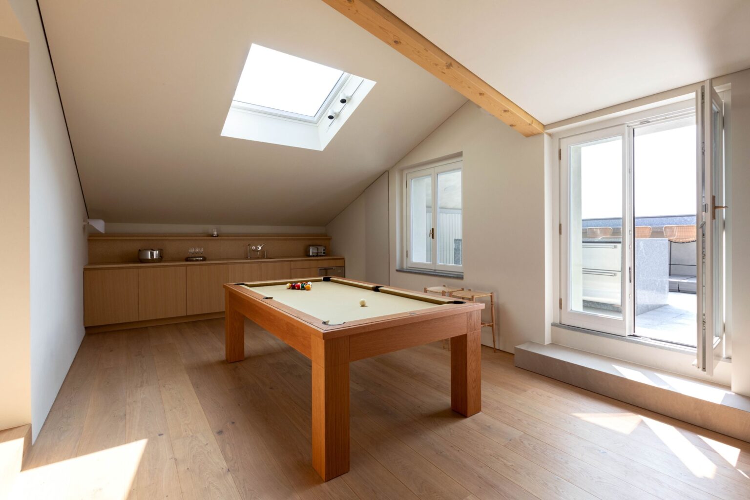 Bright and spacious attic game room featuring a wooden billiards table, large skylight, and access to a balcony through double doors, ideal for relaxation and entertainment. | Only on SopranoVillas