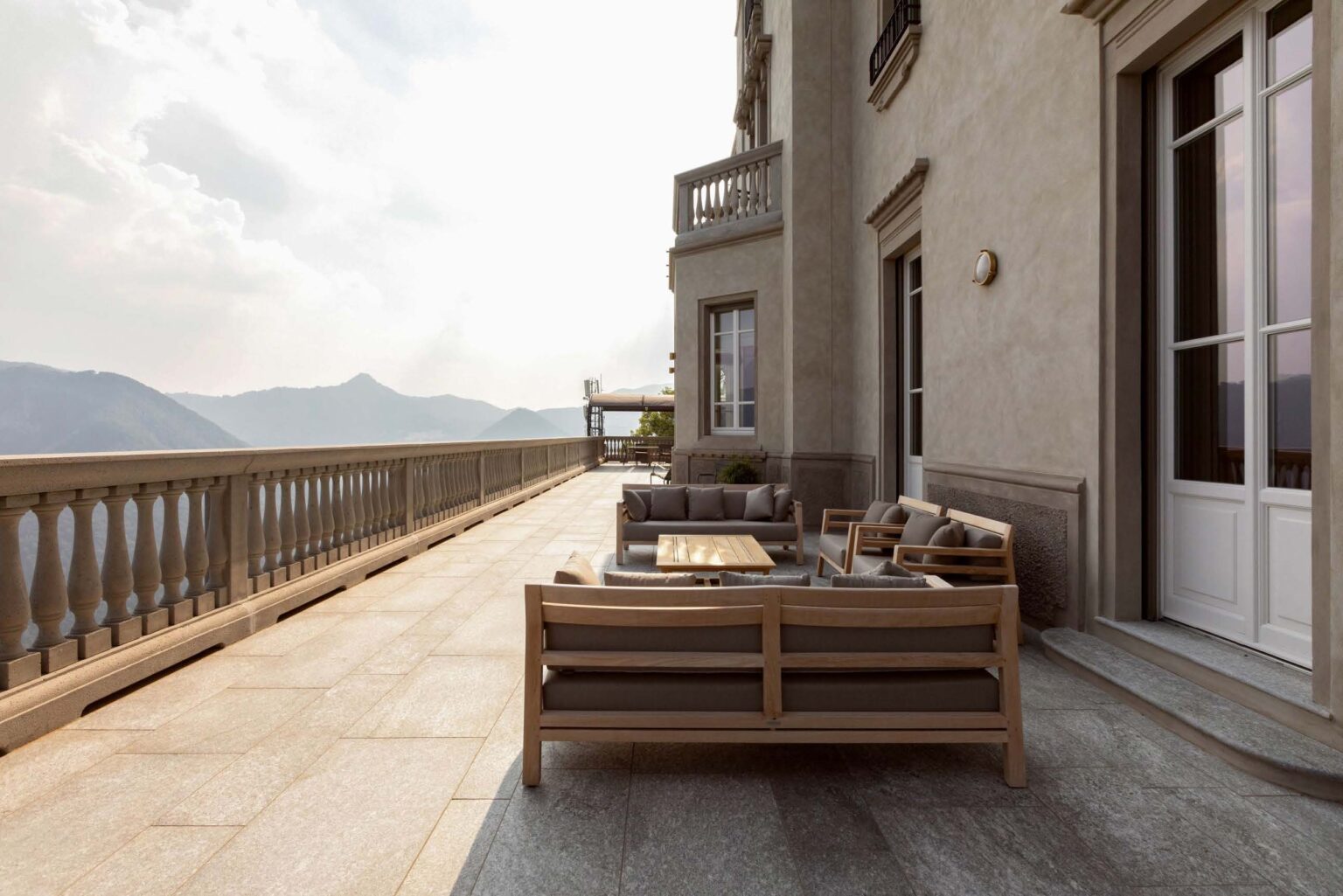 Elegant outdoor terrace featuring stylish wooden furniture, overlooking scenic mountains under a soft cloudy sky. Ideal for relaxation and enjoying nature. | Only on SopranoVillas