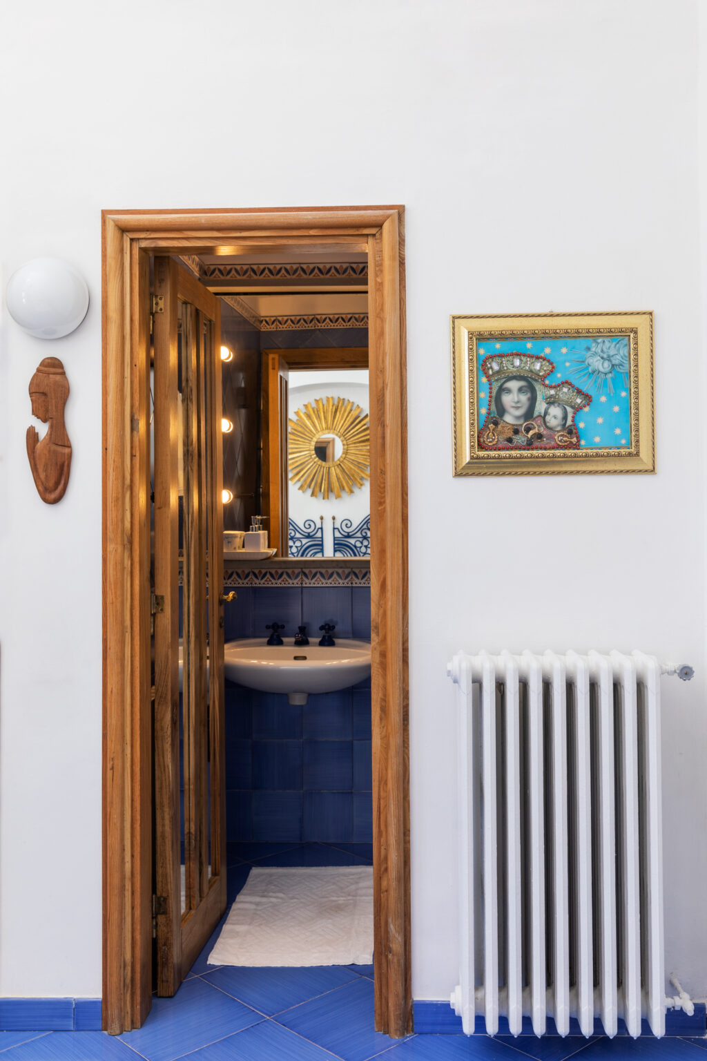 Interior view of a stylish bathroom featuring a modern sink, decorative wall art, and a wooden door with glass panels, showcasing a blend of contemporary and artistic design elements. | Only on SopranoVillas