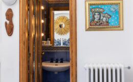 Interior view of a stylish bathroom featuring a modern sink, decorative wall art, and a wooden door with glass panels, showcasing a blend of contemporary and artistic design elements.