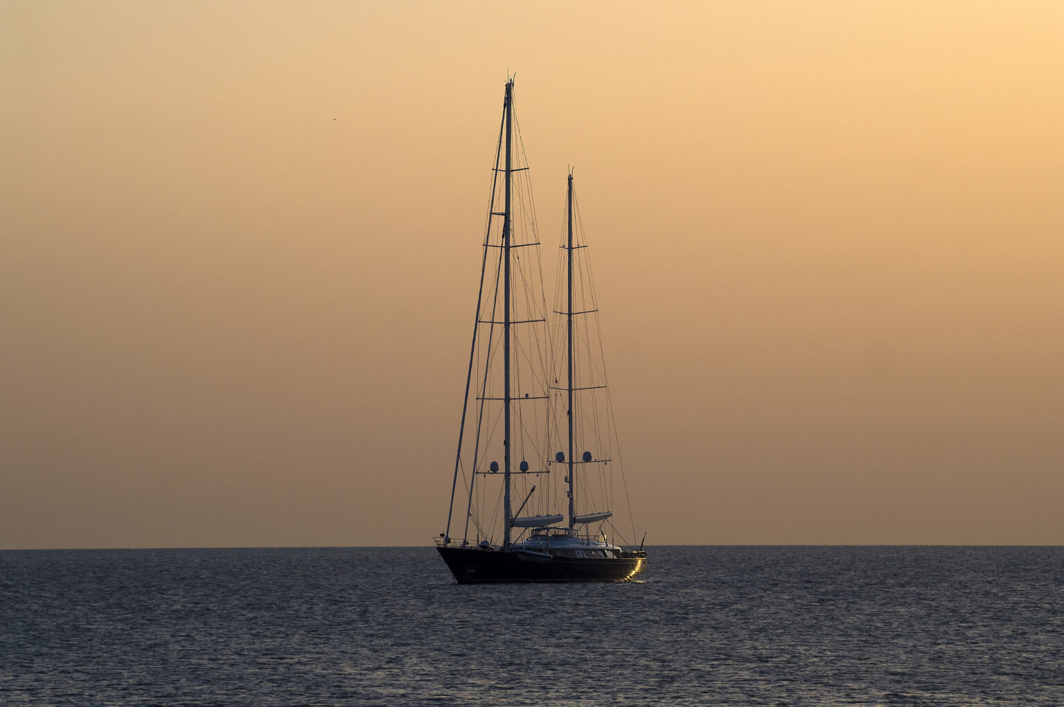 Sailing yacht on calm waters at sunset, with a gradient sky featuring warm hues of orange and yellow. | Only on SopranoVillas