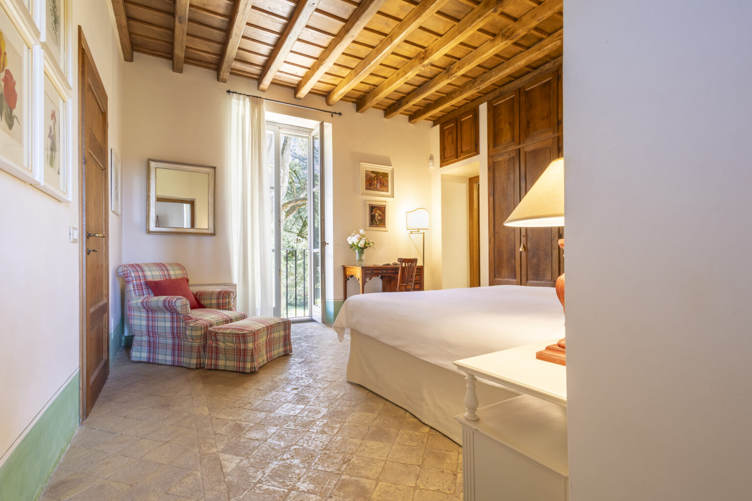 Cozy bedroom with a wooden ceiling, featuring a large bed, a plaid armchair, and natural light streaming through a window, creating a warm and inviting atmosphere. | Only on SopranoVillas