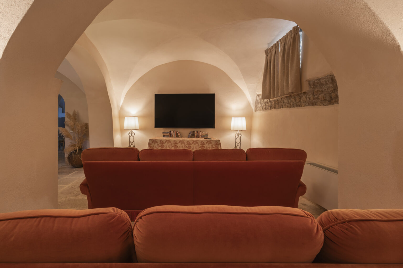 Cozy living room with an orange sofa facing a wall-mounted television, featuring arched ceilings and soft lighting for a warm ambiance. | Only on SopranoVillas