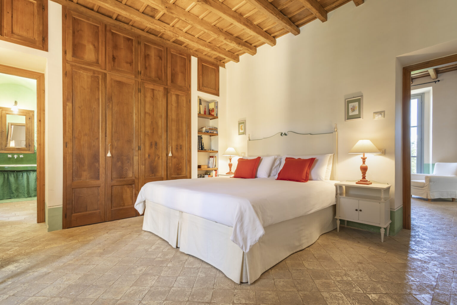 Cozy bedroom featuring a large bed with white linens and red accent pillows, wooden ceiling beams, and rustic wooden closet doors, creating a warm and inviting atmosphere. | Only on SopranoVillas