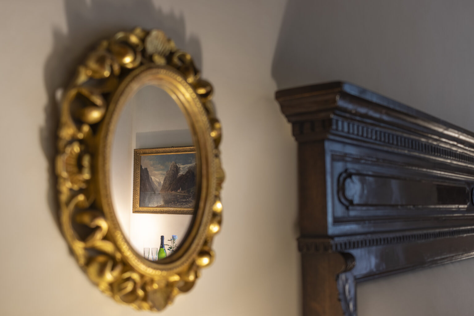 Ornate gold-framed mirror reflecting a painting and wooden mantelpiece in a softly lit room, showcasing classic interior design elements. | Only on SopranoVillas