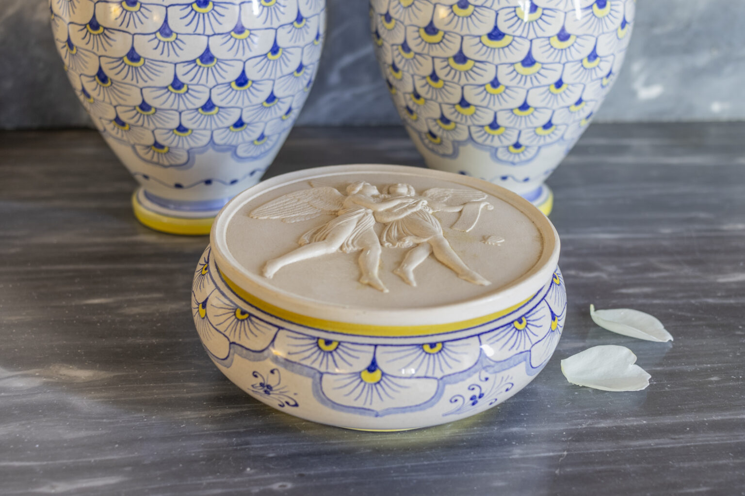 Decorative ceramic bowl with intricate blue and yellow patterns, featuring a detailed lid design, placed on a marble surface alongside two matching vases and delicate flower petals. | Only on SopranoVillas