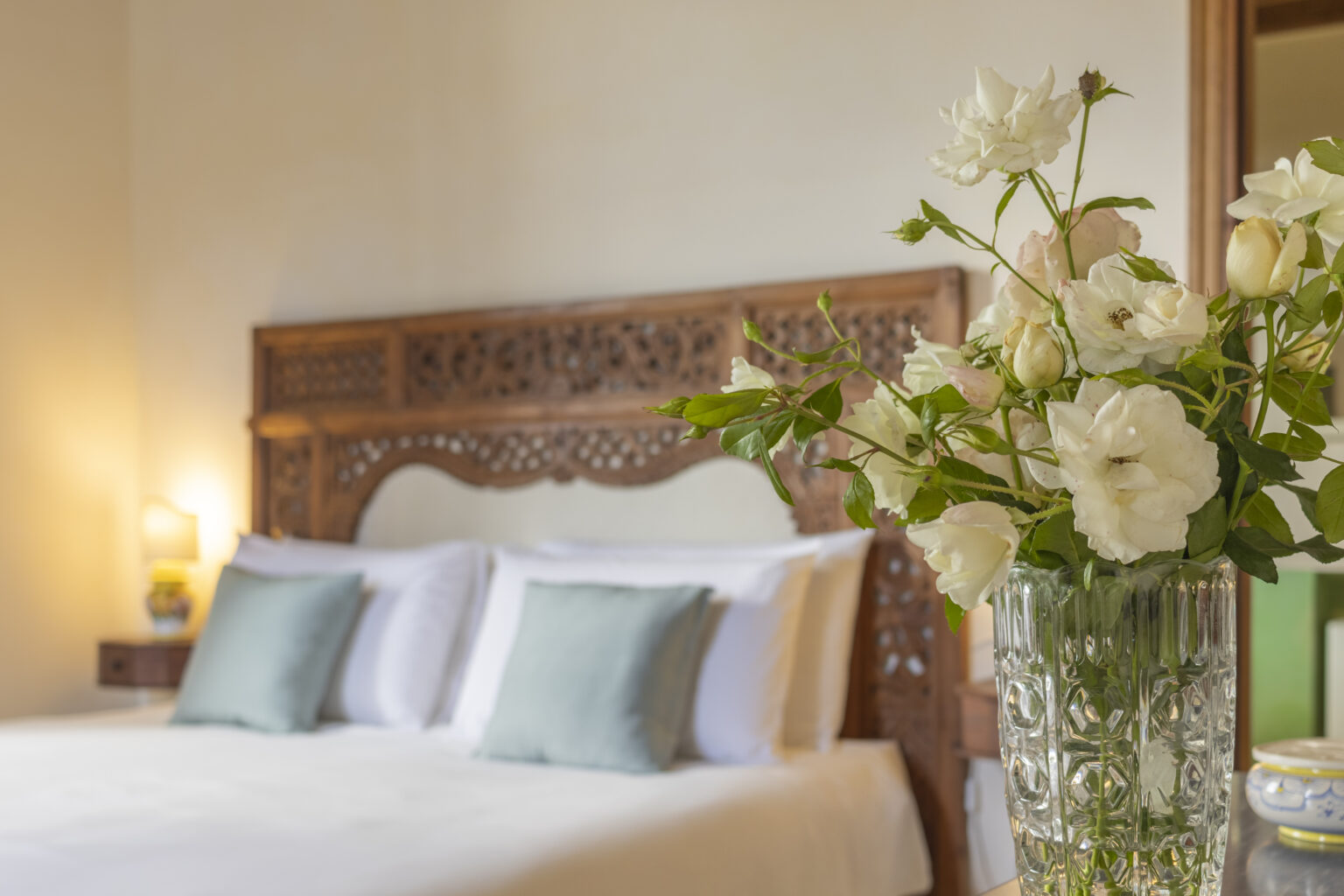 Cozy bedroom featuring a wooden headboard, white bedding with decorative pillows, and a vase of fresh white flowers on a bedside table, creating a serene and inviting atmosphere. | Only on SopranoVillas