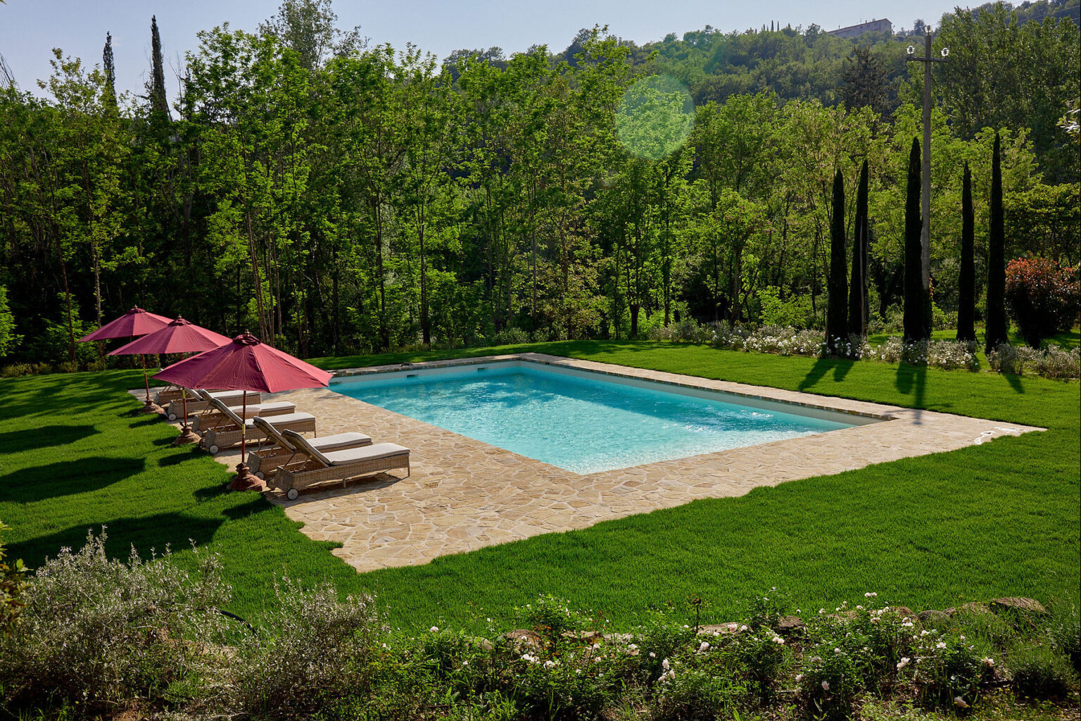 Outdoor swimming pool surrounded by lush greenery and sun loungers with pink umbrellas, ideal for relaxation and leisure in a serene setting. | Only on SopranoVillas