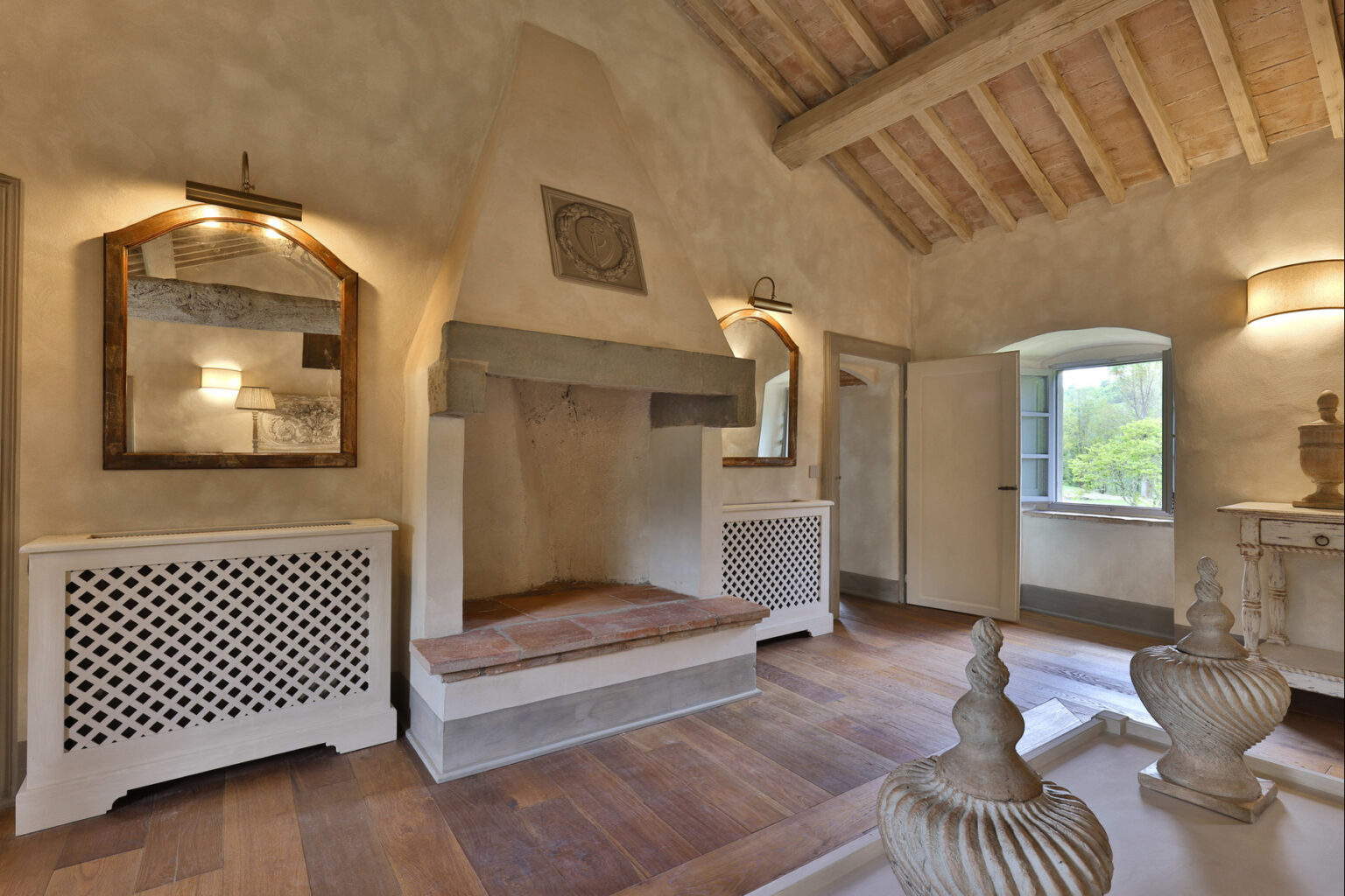 Cozy interior of a rustic living room featuring a stone fireplace, wooden beams, and decorative accents, with natural light coming through a window. | Only on SopranoVillas