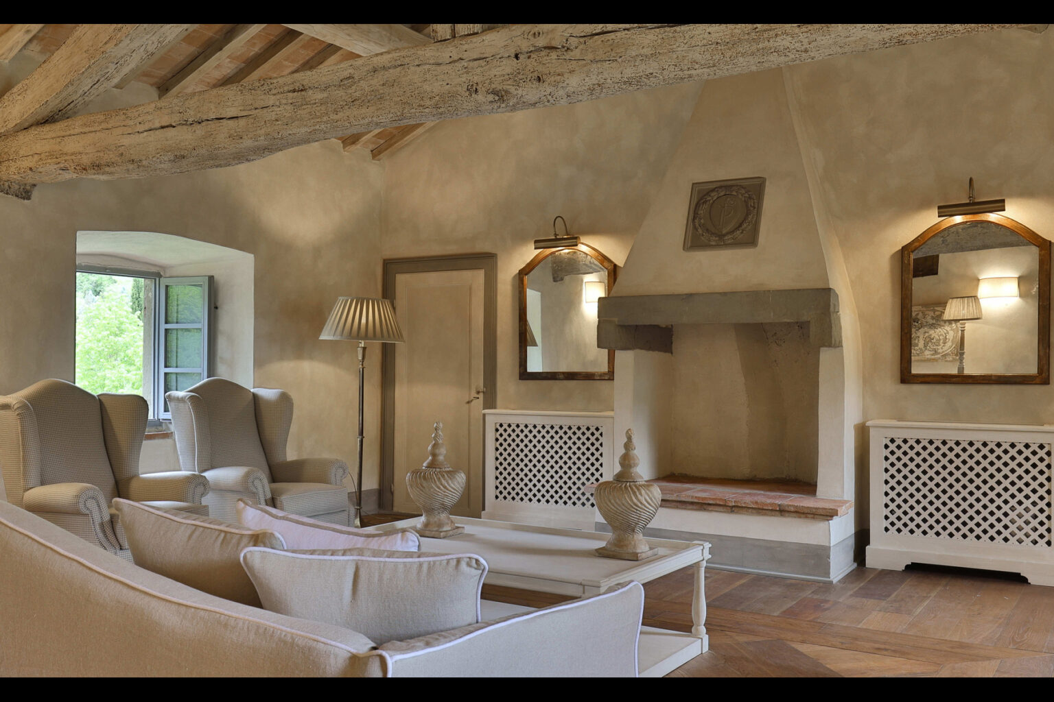 Cozy living room interior featuring rustic wooden beams, elegant armchairs, a decorative fireplace, and large windows allowing natural light. The room is adorned with mirrors and stylish decor, creating a warm and inviting atmosphere. | Only on SopranoVillas