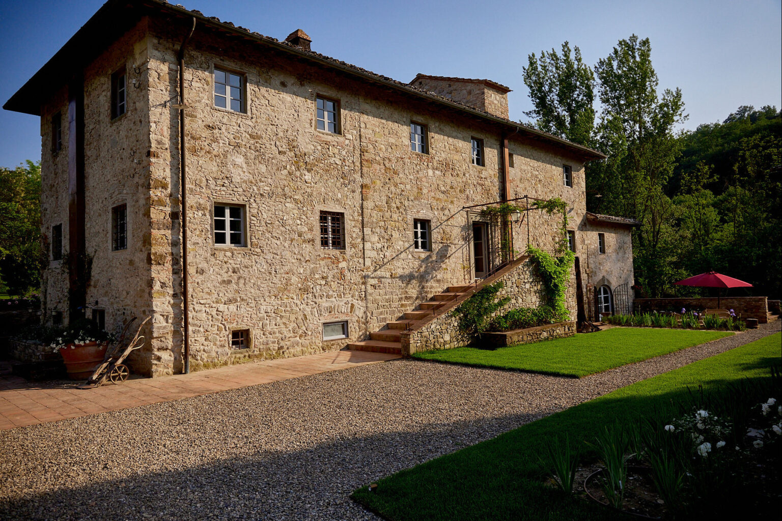 Historic stone villa surrounded by greenery, featuring a landscaped yard with a gravel pathway and stairs leading to the entrance. | Only on SopranoVillas