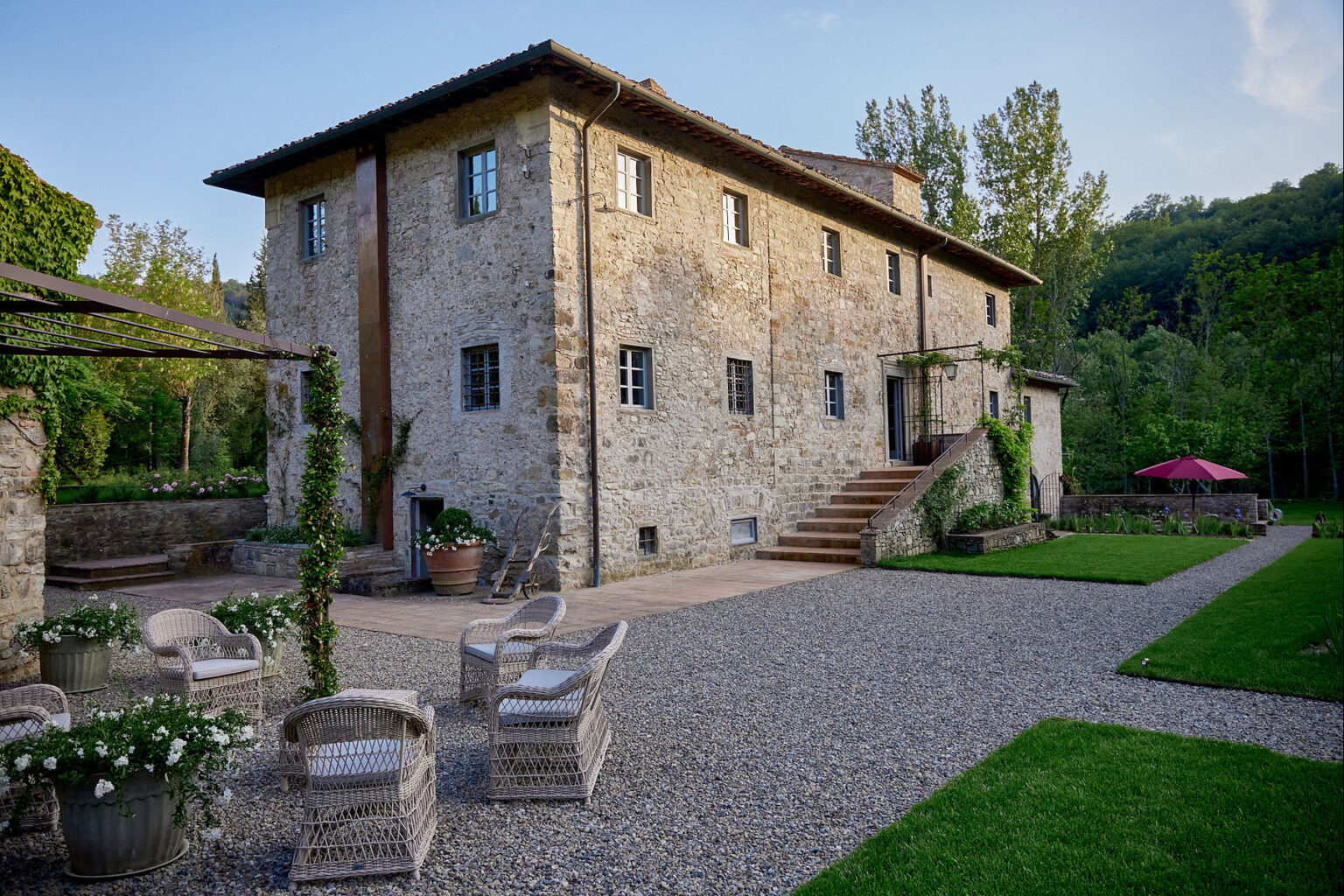 Rustic stone farmhouse surrounded by lush greenery, featuring a landscaped garden with gravel pathways, outdoor seating, and a staircase leading to the entrance. Ideal for vacation rentals or countryside retreats. | Only on SopranoVillas