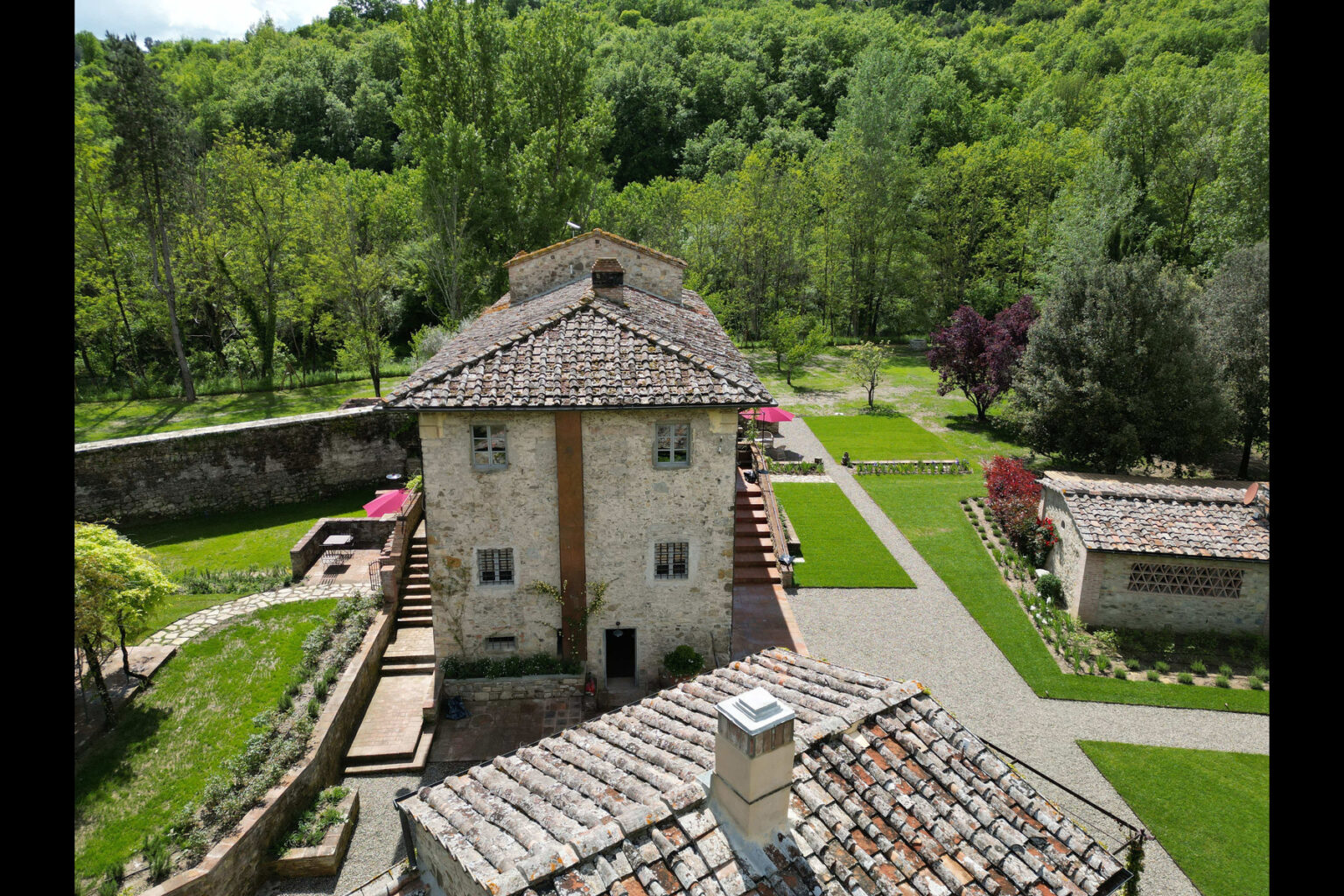 Aerial view of a rustic stone villa surrounded by lush greenery and landscaped gardens, featuring a traditional tiled roof and outdoor seating areas. | Only on SopranoVillas
