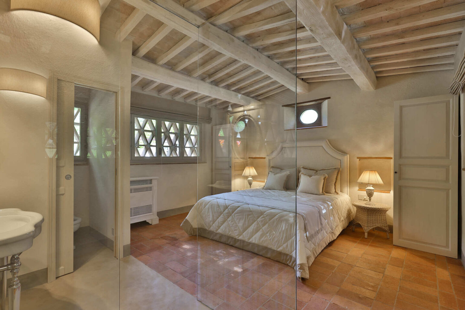 Cozy bedroom with rustic wooden beams, elegant furnishings, and large windows allowing natural light, featuring a plush bed, bedside lamps, and a stylish decor. | Only on SopranoVillas