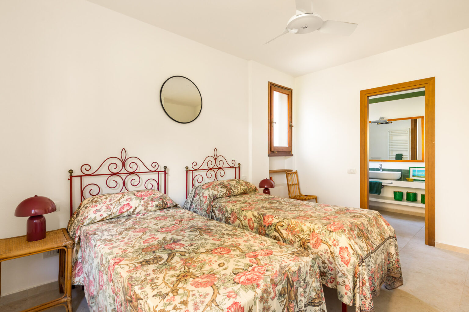 Cozy bedroom featuring two twin beds with floral bedspreads, a decorative mirror on the wall, and a doorway leading to a bathroom. The room is well-lit and has a minimalist design, ideal for a comfortable stay. | Only on SopranoVillas