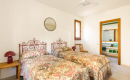 Cozy bedroom featuring two twin beds with floral bedspreads, a decorative mirror on the wall, and a doorway leading to a bathroom. The room is well-lit and has a minimalist design, ideal for a comfortable stay.
