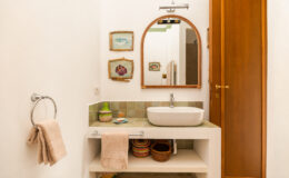 Modern bathroom interior featuring a round mirror above a stylish sink, decorative wall art, and neatly arranged towels. The design includes wooden elements and a clean, minimalist aesthetic.