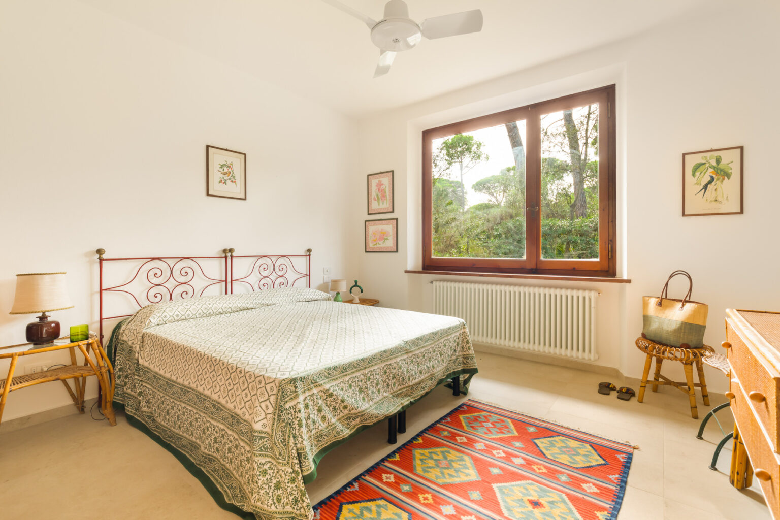 Cozy bedroom featuring a double bed with a patterned bedspread, large window with views of greenery, light-colored walls, wooden furniture, and a decorative rug. Ideal for relaxation and comfort. | Only on SopranoVillas