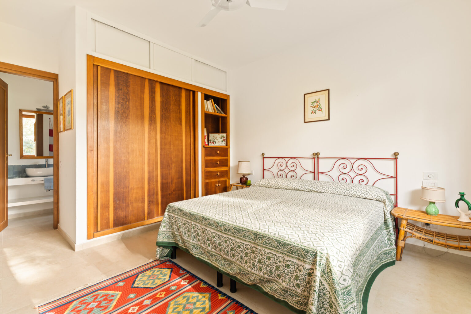 Cozy bedroom featuring a wrought iron bed with a green patterned bedspread, wooden wardrobe, and a side table. The room has a warm, inviting atmosphere with natural light illuminating the space. | Only on SopranoVillas