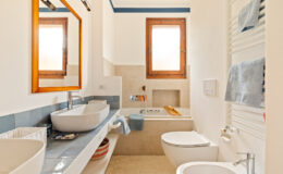 Modern bathroom with natural light, featuring a stylish sink, a bathtub, and a wooden-framed mirror. The space is decorated with blue and neutral tones, creating a calming atmosphere.