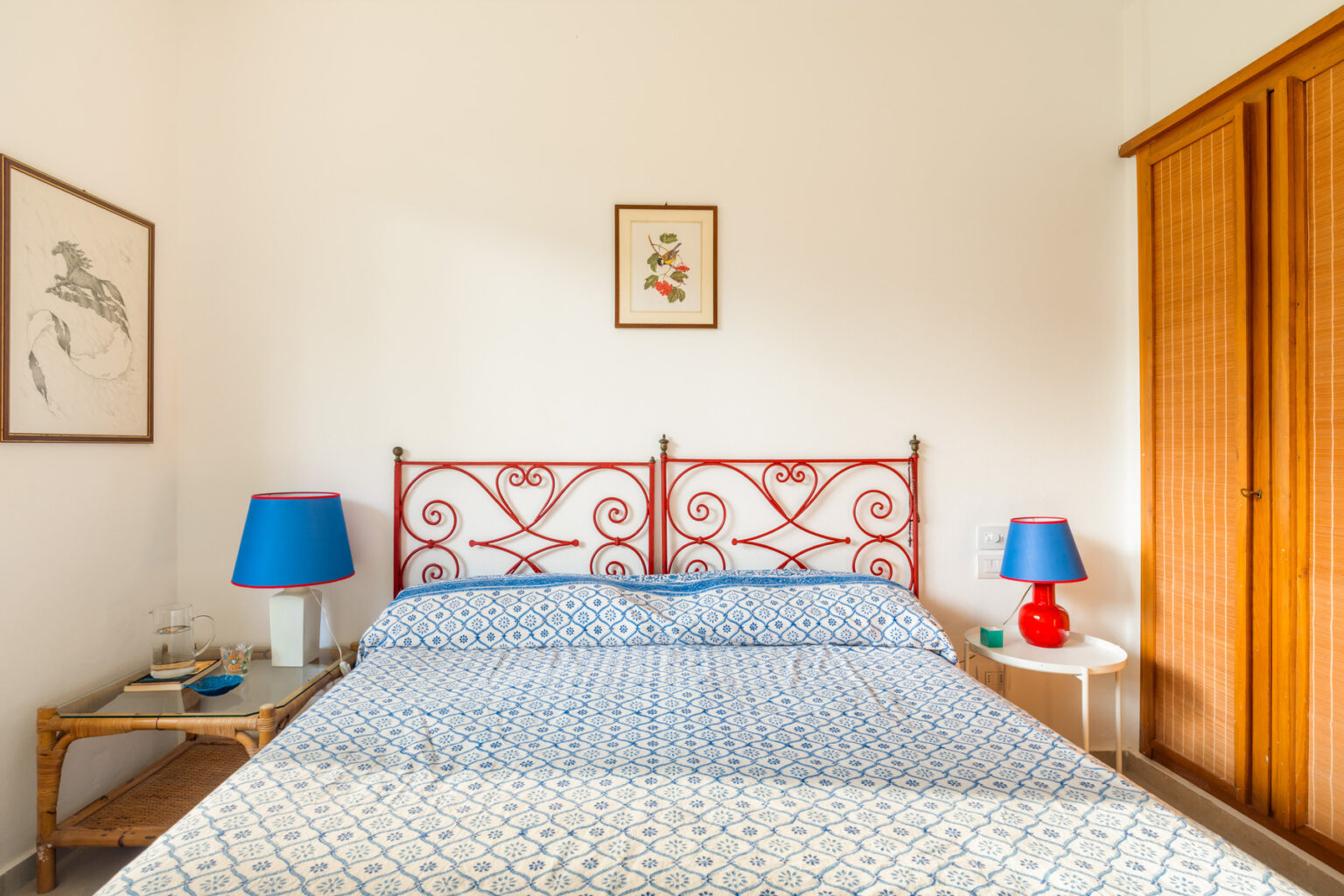 Cozy bedroom featuring a wrought iron bed with decorative headboard, blue and white patterned bedding, bedside tables with lamps, and a wooden wardrobe, creating a warm and inviting atmosphere. | Only on SopranoVillas