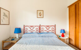 Cozy bedroom featuring a wrought iron bed with decorative headboard, blue and white patterned bedding, bedside tables with lamps, and a wooden wardrobe, creating a warm and inviting atmosphere.
