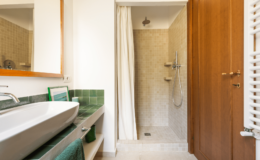Modern bathroom interior featuring a sleek sink with green accents, a spacious shower area with a glass door, and wooden cabinetry. Natural light enhances the clean design and neutral color palette.