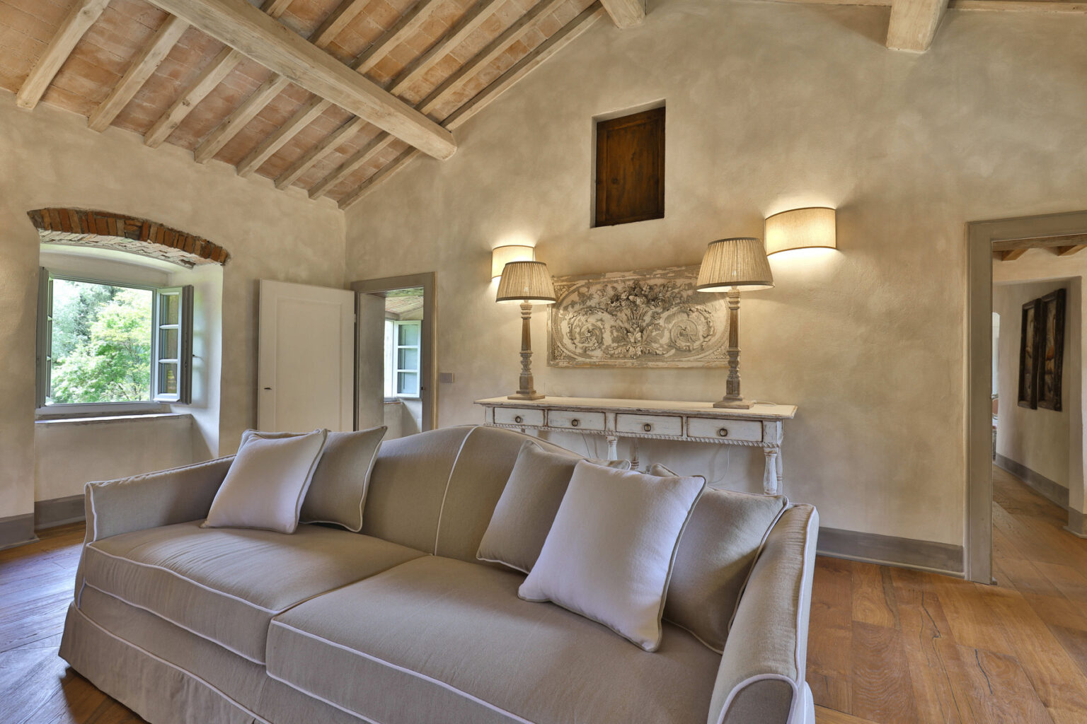 Cozy living room featuring a light gray sofa with decorative pillows, elegant wall art, and warm wooden beams, creating a welcoming atmosphere with natural light from the windows. | Only on SopranoVillas