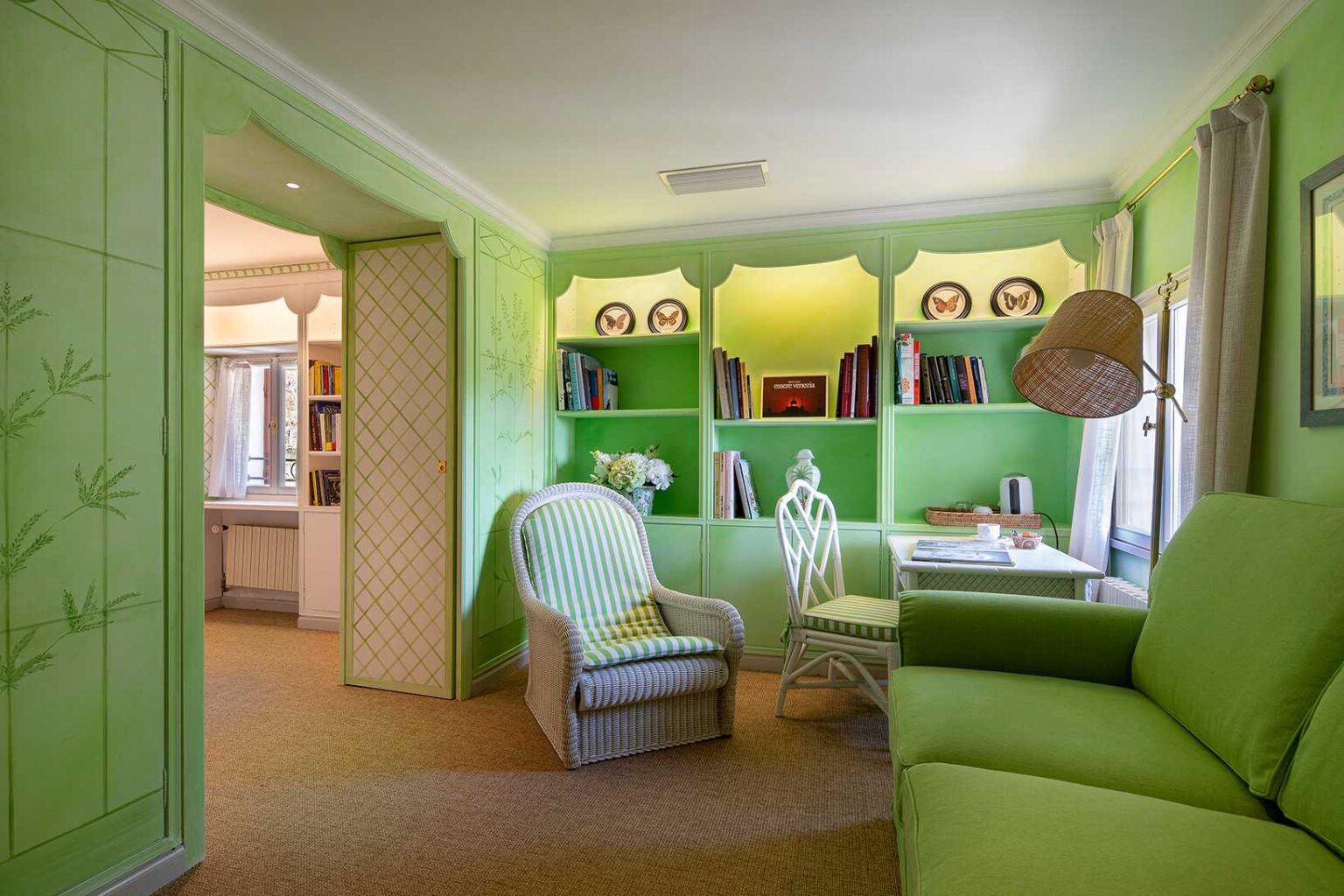 Bright and inviting green-themed room featuring a cozy seating area with a green sofa and striped armchair, surrounded by built-in shelves filled with books and decorative items. Natural light streams in through the window, enhancing the vibrant decor. | Only on SopranoVillas