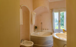 Modern bathroom featuring a curved bathtub, bidet, and elegant decor with a soft pink color scheme. Natural light filters through a window, illuminating the space and highlighting the stylish fixtures and towels.