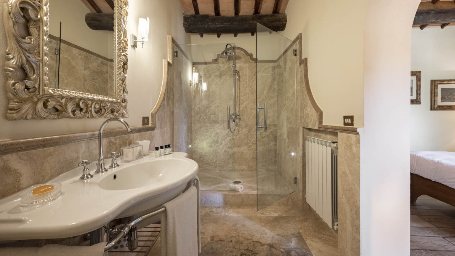 Luxurious bathroom featuring a stylish marble sink, ornate mirror, and a spacious glass-enclosed shower. The elegant design includes warm lighting and tasteful decor, creating a serene atmosphere. | Only on SopranoVillas