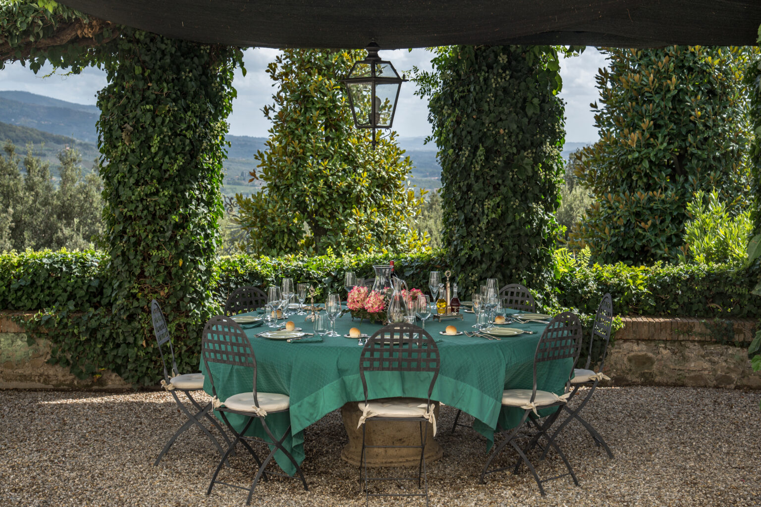 Elegant outdoor dining setup featuring a green tablecloth and stylish black chairs, surrounded by lush greenery and a scenic view, perfect for al fresco gatherings. | Only on SopranoVillas