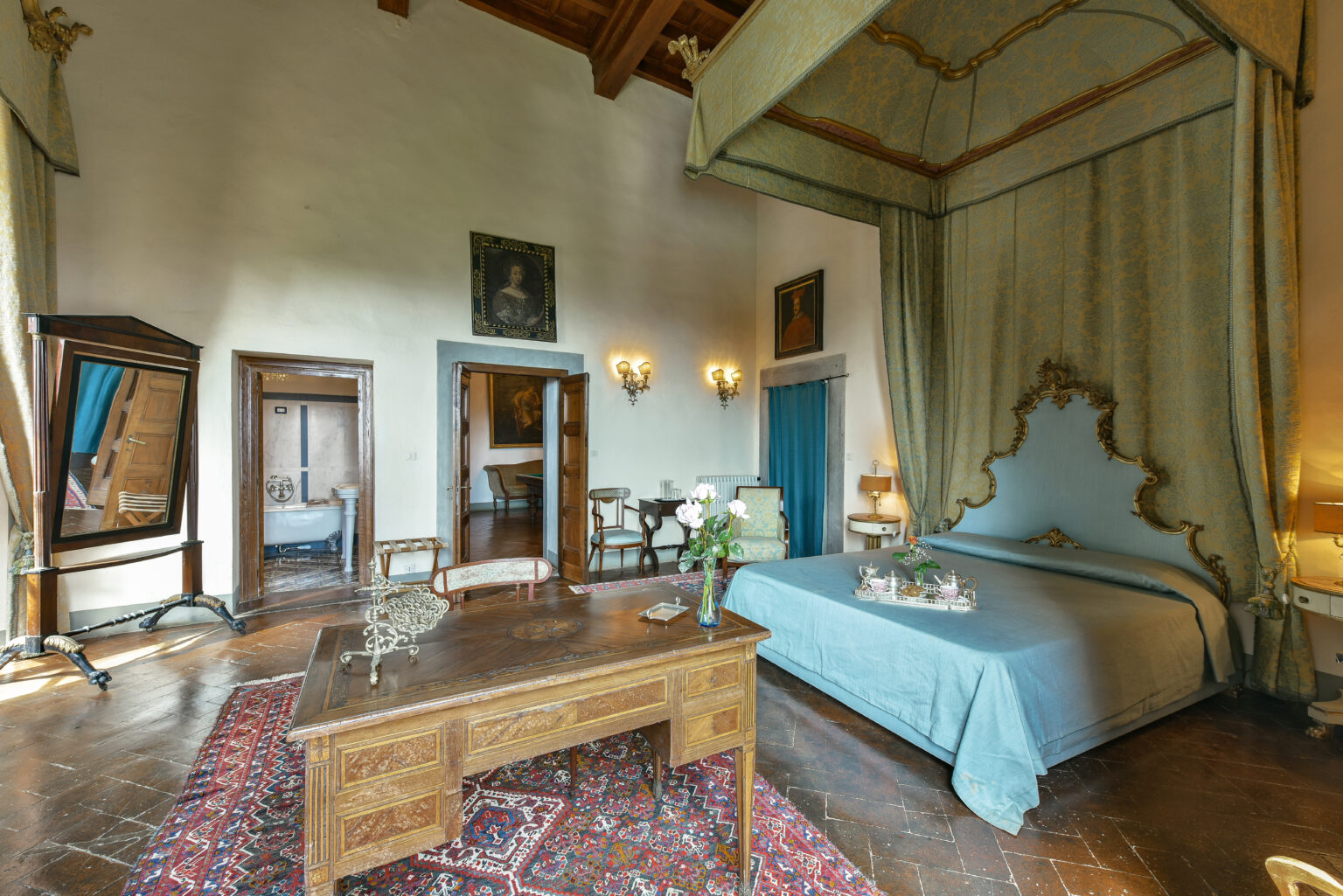 Luxurious bedroom featuring a blue canopy bed, elegant wooden furniture, and vintage decor. The room is illuminated by natural light, highlighting the ornate ceiling and rich textures of the furnishings. Ideal for showcasing upscale accommodation options. | Only on SopranoVillas