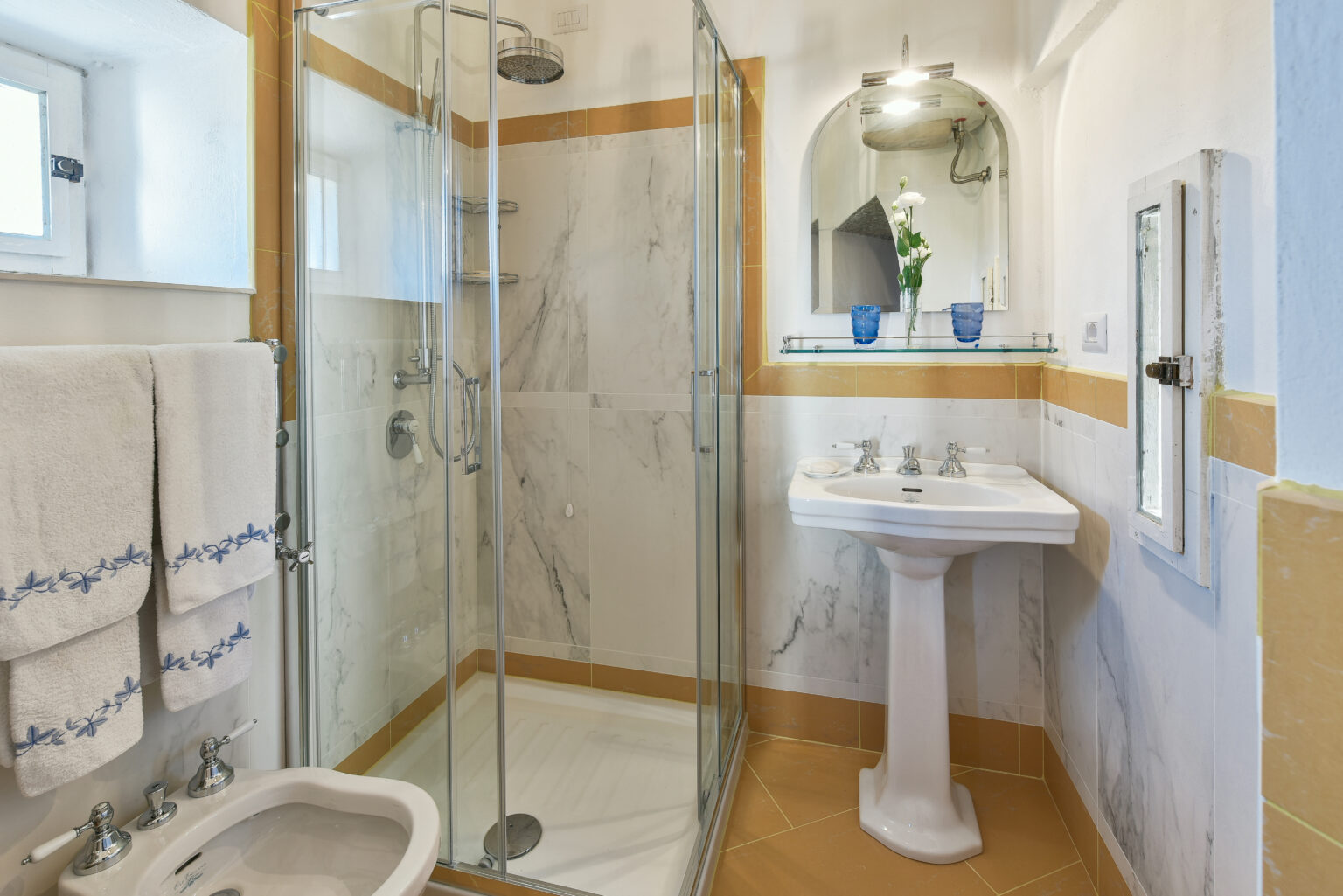 Modern bathroom featuring a glass shower enclosure, elegant marble walls, a pedestal sink, and neatly arranged towels, creating a stylish and functional space. | Only on SopranoVillas